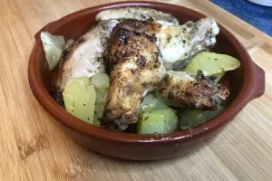 Alitas de pollo asadas al horno y acompañadas de patatas. Servidas en un cuenco de barro