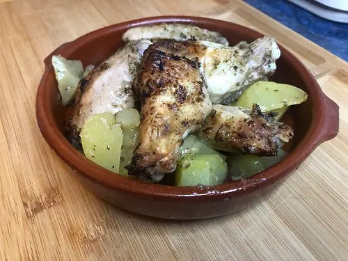 Alitas de pollo asadas al horno y acompañadas de patatas. Servidas en un cuenco de barro