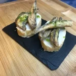 Boquerones fritos servidos con salsa verde y limón sobre pan tostado