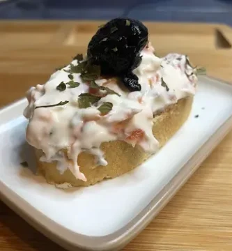 Montadito con ensaladilla de palitos de cangrejo, decorada con aceituna negra y perejil.